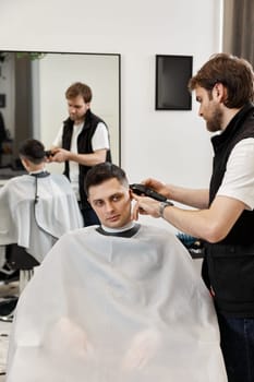 Barber shaving handsome caucasian man in barber shop.