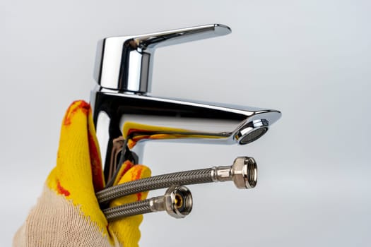 a shiny new sink faucet in the hand of a gloved plumber. Sink mixer before installation. Hot and cold water supply hoses are visible. the mounting screw for mounting is visible.