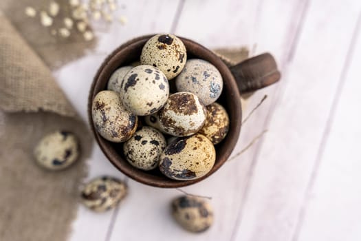 Fresh quail eggs in a clay mug on the table. Bright spring festive background and a branch of gypsophila. Close-up. Healthy eating. Easter. top view