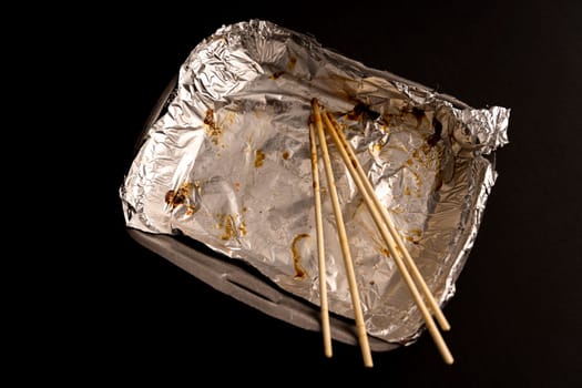 An empty plastic container for the delivery of a set of sushi. Chopsticks and an empty thermobox with foil inside for a set of sushi on a dark background. lunch. View from above. Flat lay. Copy space