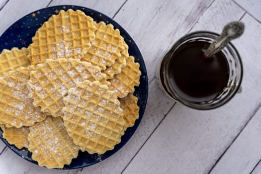 sweet delicious crispy waffles sprinkled with powdered sugar and a glass of tea in a vintage cup holder. Breakfast by the window. Top view