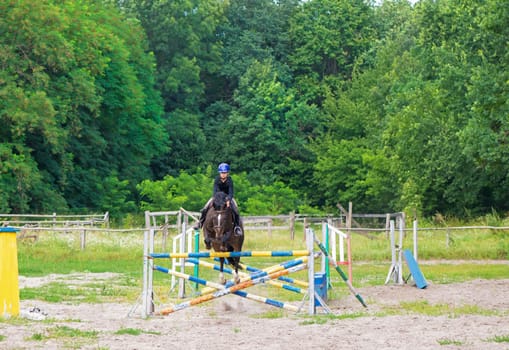 Young rider on horse jumping over obstacle on her course in competition