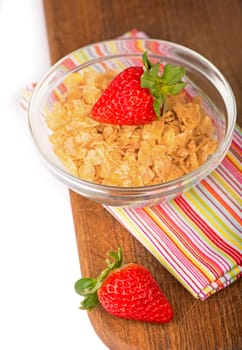 Bowl of tasty crispy corn flakes with milk and strawberries on white