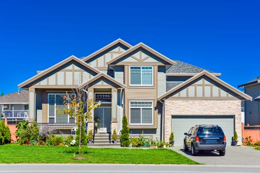 A perfect neighbourhood. Brand new residential house with car parked on driveway in front. Big family house with double garage door and blue sky background. British Columbia, Canada