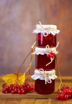 Viburnum fruit jam in a glass jar on a wooden table, preparations for the winter