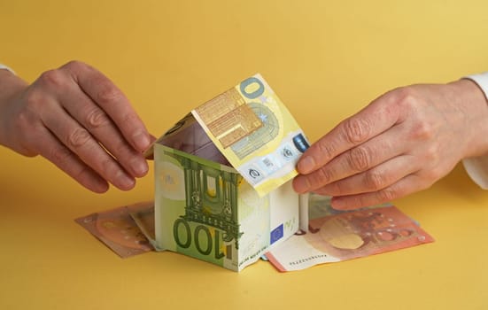 Businessman's hand holding house made of euro notes on table