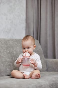 cute baby girl holding bottle and drinking water at home.