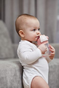 cute baby girl holding bottle and drinking water at home.