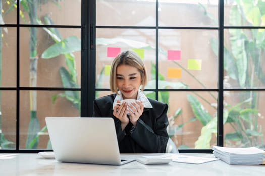 Smiling business woman drinking coffee while working on laptop from office.