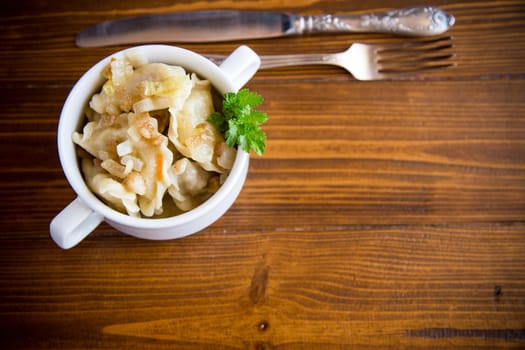 cooked dumplings with potatoes and fried onions, in a bowl on a wooden table.