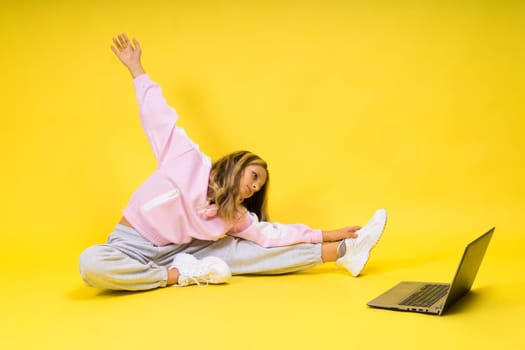 Fitness online. Girl doing stretching exercise on a floor alone with laptop at studio