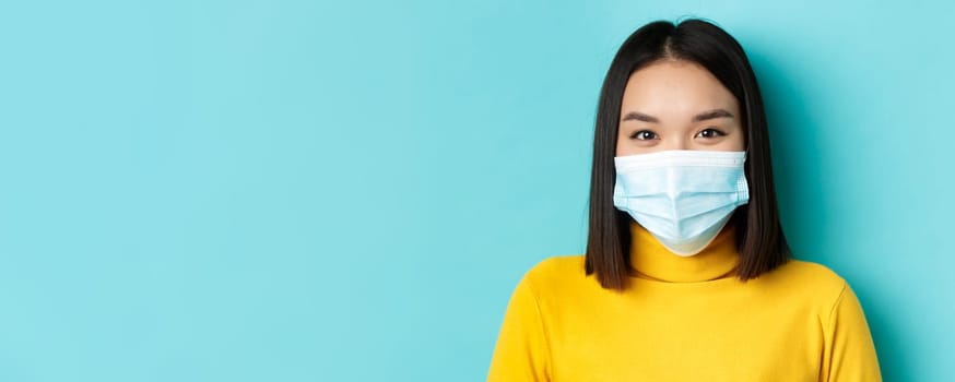 Covid-19, social distancing and pandemic concept. Close up of young asian woman with short dark hair, wearing medical mask and smiling with eyes, looking hopeful at camera.