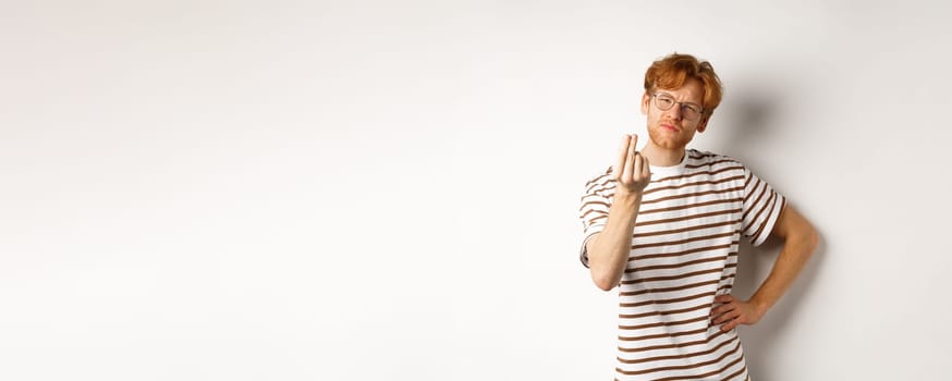 Image of satisfied young man with red hair and glasses showing chefs kiss gesture to praise something perfect, standing over white background.