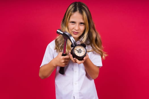 Young blonde girl holding an alarm clock and hammer smiling and laughing hard out loud.