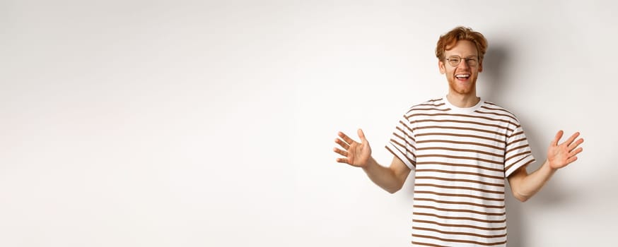 Attractive young man with red hair and glasses showing large size, length of big object, smiling satisfied, standing over white background.