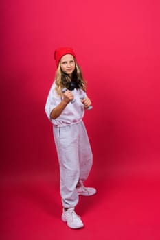 Kid girl doing fitness exercises with dumbbells on a red background