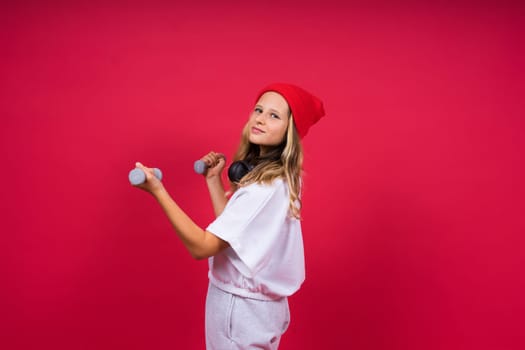 Kid girl doing fitness exercises with dumbbells on a red background