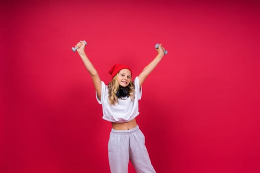 Kid girl doing fitness exercises with dumbbells on a red background