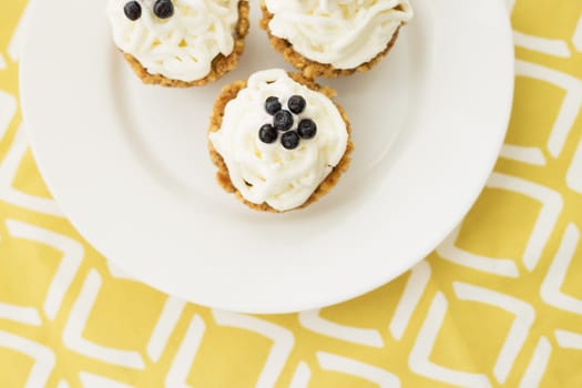 Homemade muffins with blueberries, cream and fresh berries on a yellow napkin.