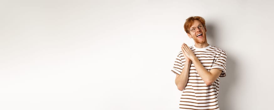 Happy redhead man clap hands and looking satisfied at upper right corner, getting ready for something, standing over white background.