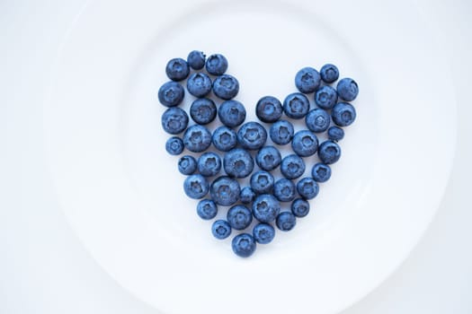 ripe blueberries in a heart shape on a white plate.