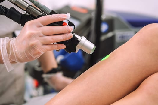 Close up shot of gloved hand with the laser hair removal machine's handpiece along woman leg. Alexandrite laser techhnology removing hair. Beauty procedureBeauty technology concept