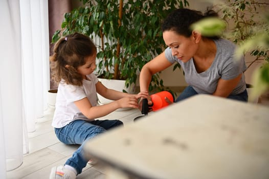 Selective focus on mother and daughter caring for houseplants, watering soil with repotted houseplants, sitting together on floor at home veranda in spring. Environmental conservation. People. Nature