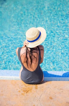 Beautiful girl in a black swimsuit near a blue pool.