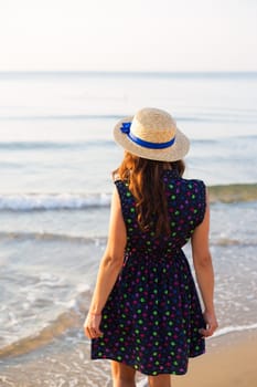 Beautiful girl in a hat stands with her back on a sandy beach