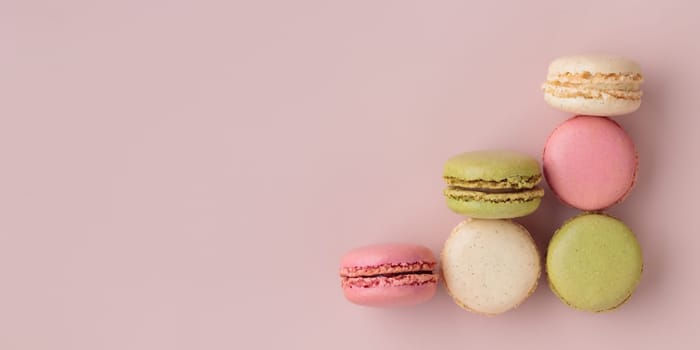 Colorful macaroons on pink background, top view, increase in profits of the confectionery production horizontal banner