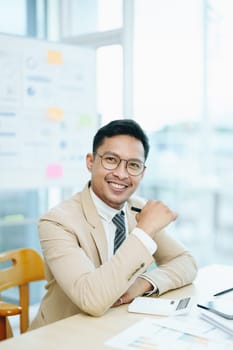 Portrait of a male business owner showing a happy smiling face as he has successfully invested his business using computers and financial budget documents at work.