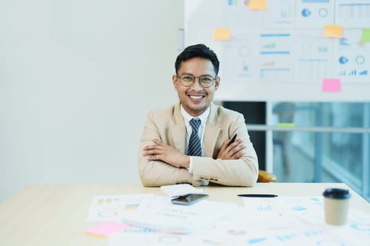 Portrait of a male business owner showing a happy smiling face as he has successfully invested his business using computers and financial budget documents at work.