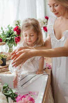 A little blonde girl with her mom on a kitchen countertop decorated with peonies. The concept of the relationship between mother and daughter. Spring atmosphere.