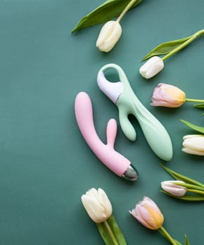 Two toys for adults lie on a green background, surrounded by tulips