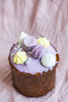 A traditional paska decorated with white Swiss chocolate and meringue stands on a lavender tablecloth. Easter holiday