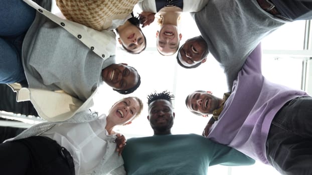 Closeup portrait, bottom view, happy faces of different team employees standing in circle, looking at camera, smiling business women and businessmen doing team building, posing for photo