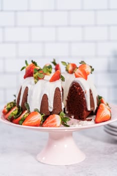 Slicing red velvet bundt cake with cream cheese frosting garnished with fresh strawberries.