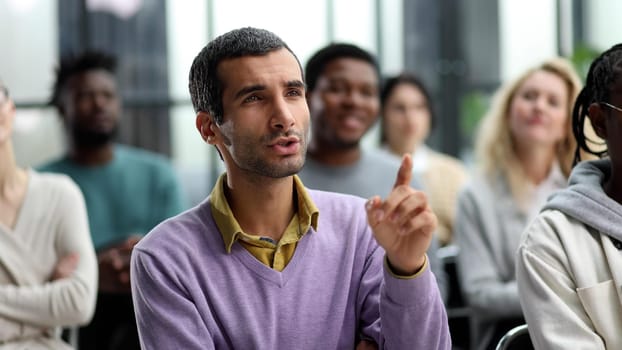 Group of young people sitting on conference together while one man raising his hand