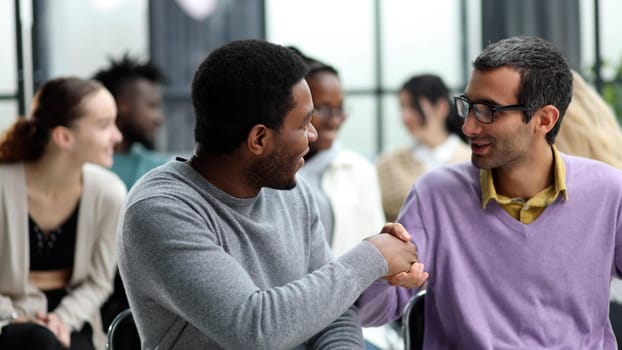 Diverse people sitting in circle holding hands at group therapy