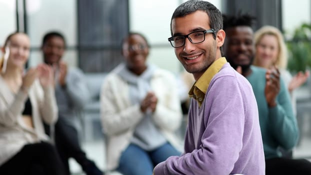 Young businessman sitting listening to trainer speaking to audience in trendy office