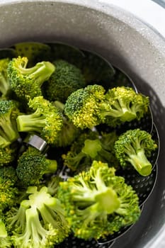 Steaming fresh broccoli in a cooking pot with a steamer basket to prepare steamed broccoli.