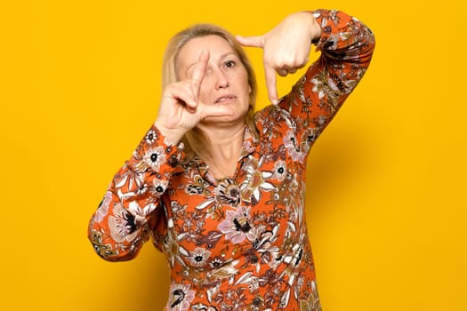 Caucasian blonde woman wearing a patterned dress making the framing gesture with a suffering face isolated on yellow studio background