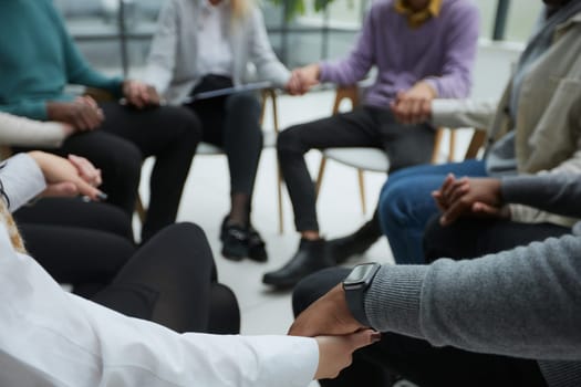 Diverse people sitting in circle holding hands at group therapy