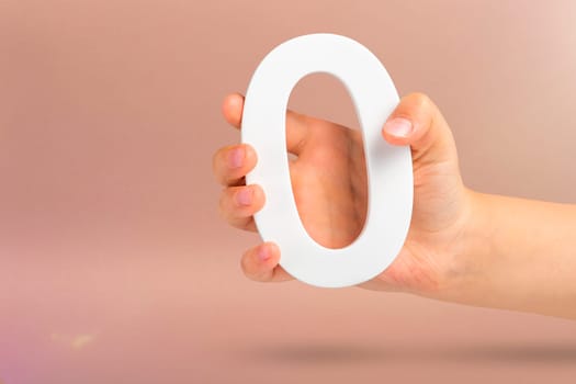 Numeral zero in hand. A hand holds a white number zero on a red background with copy space. Zero concept, 0 percent interest rate, minimum air emissions, cost or credit no increase