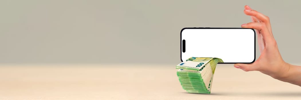 Money is falling from a mobile phone, a hand is holding a phone, a pack of 100 euro bills is sticking out of the phone. Financial investment concept from mobile app. copy space.