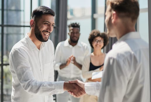 Glad to work with you. Young modern men in smart casual wear shaking hands and smiling while working in the creative office