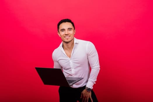 Image of young cheerful businessman holding and using laptop isolated over red background