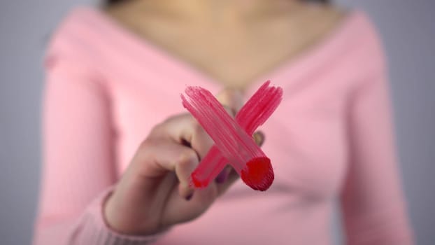 A young woman draws a red cross on the glass. A girl in a pink sweater draws with a brush and paint. Close-up. 4k