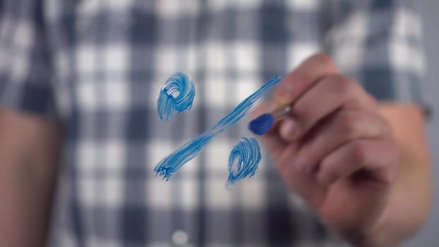 A young man draws a mathematical percent sign on the glass. A man in a shirt draws with a brush and blue paint. Close-up. 4k