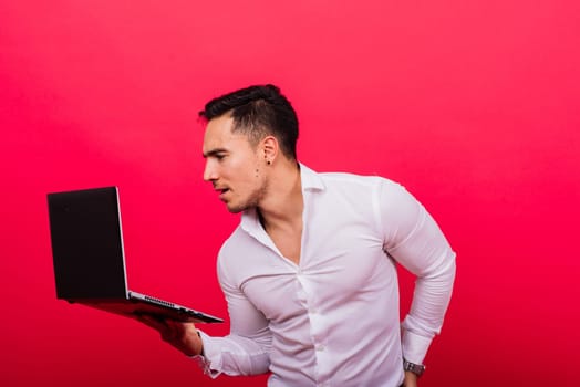 Image of young cheerful businessman holding and using laptop isolated over red background